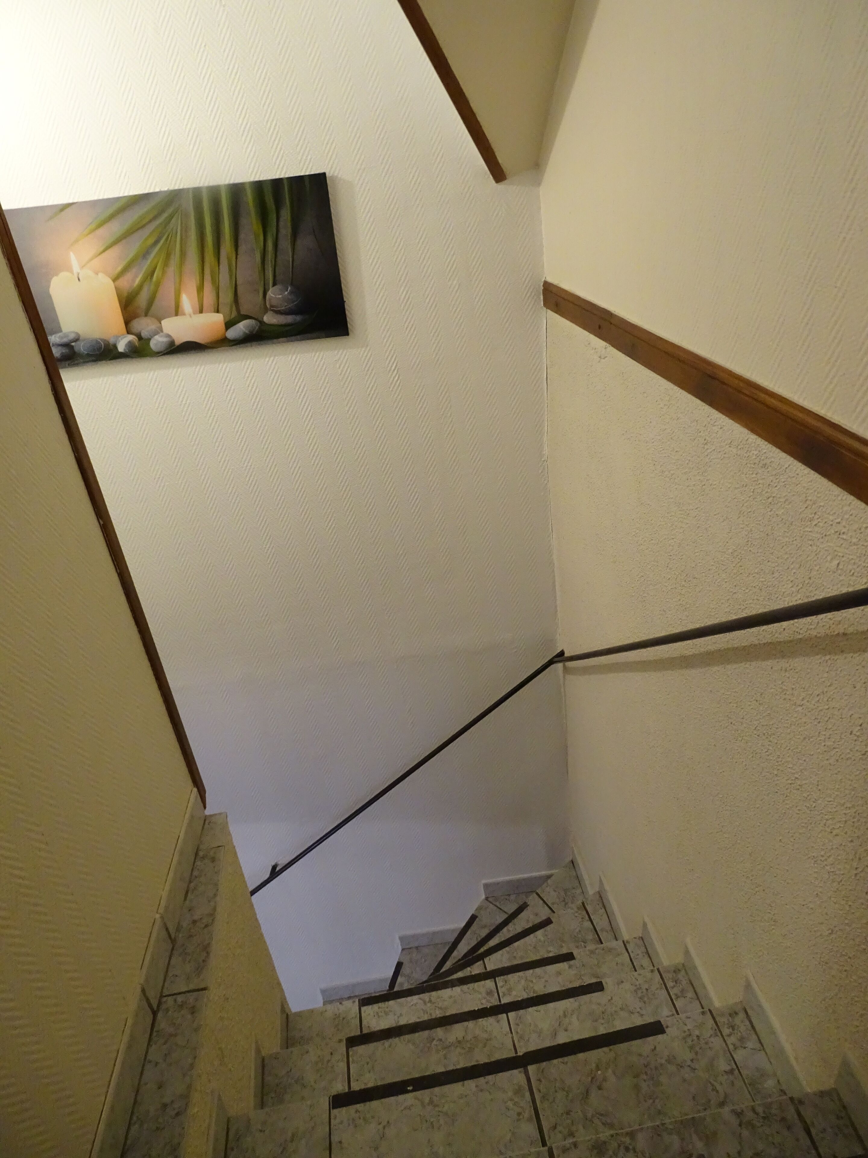 A staircase with a handrail, a painting of a candle and rocks, and a textured wall.