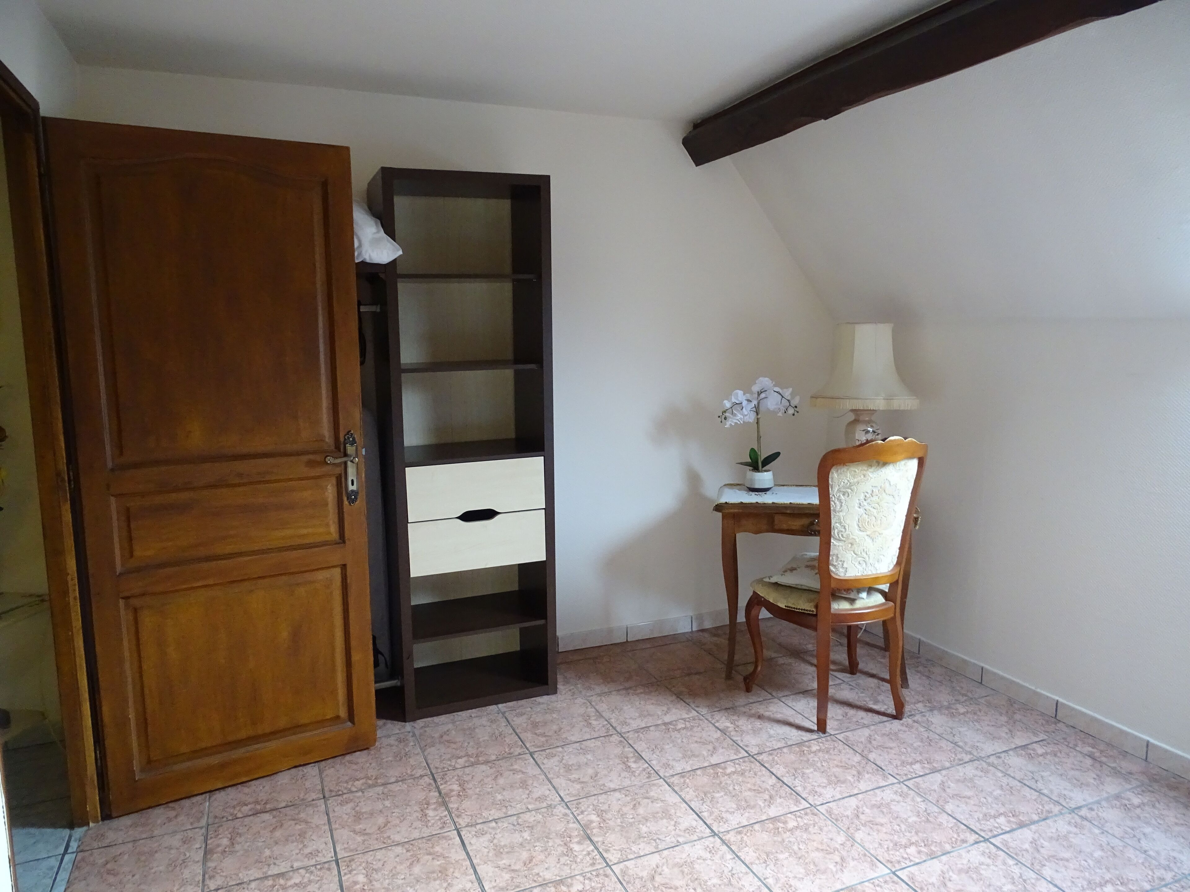 Une pièce avec une porte en bois, une bibliothèque intégrée, une petite table avec une lampe et une chaise.