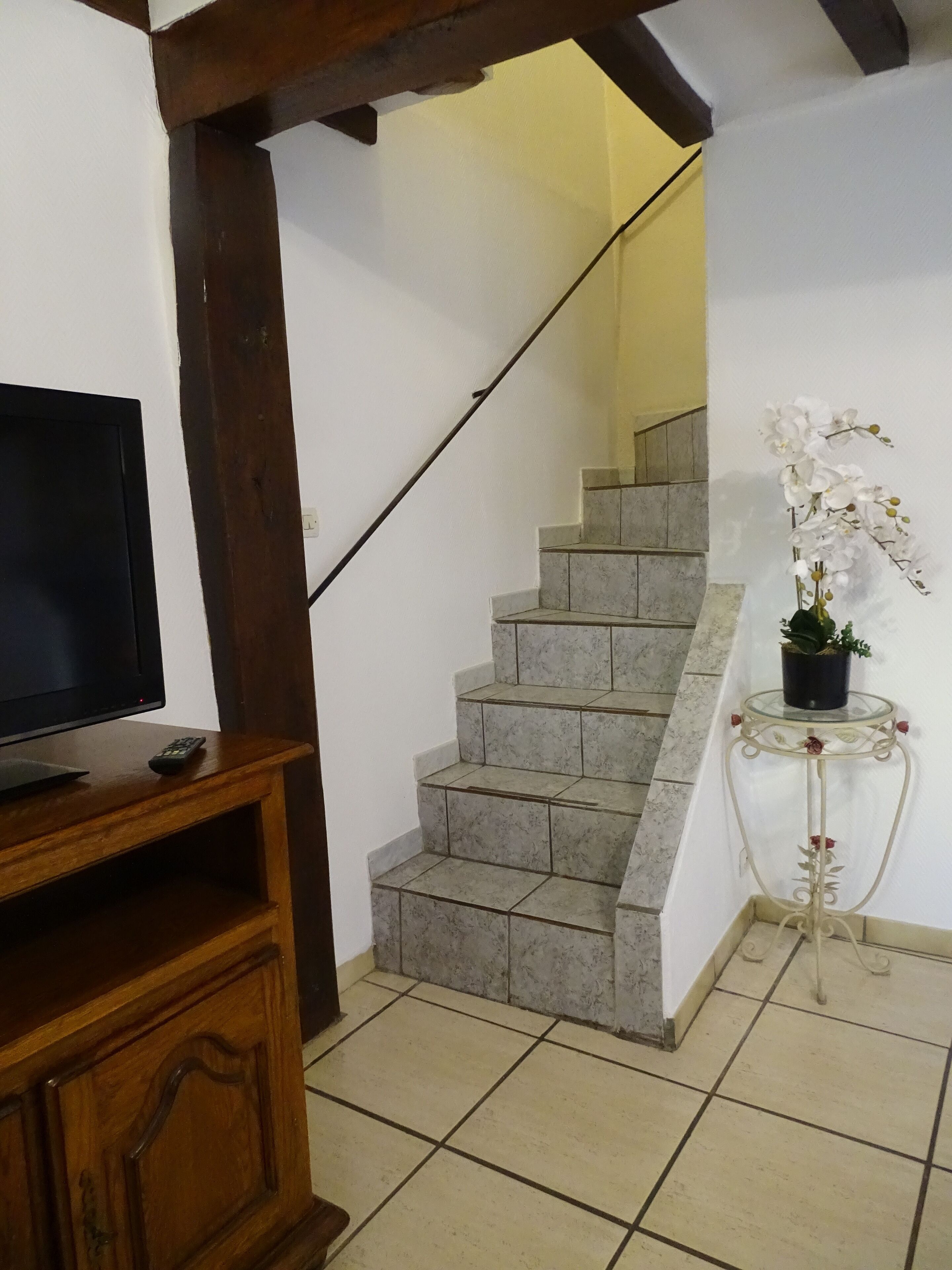 A staircase with marble steps, a wooden TV stand, and a small table with a potted orchid.
