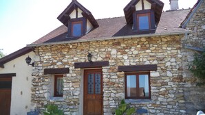 A stone house with a wooden door, two windows, and a small porch area with potted plants.