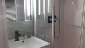 Une salle de bain moderne avec une douche à parois de verre, un lavabo blanc et un miroir au-dessus.