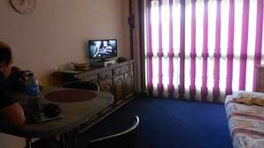 Une chambre d’hôtel équipée d’une télévision, d’une table à manger, d’un lit et d’une fenêtre avec des rideaux à rayures.