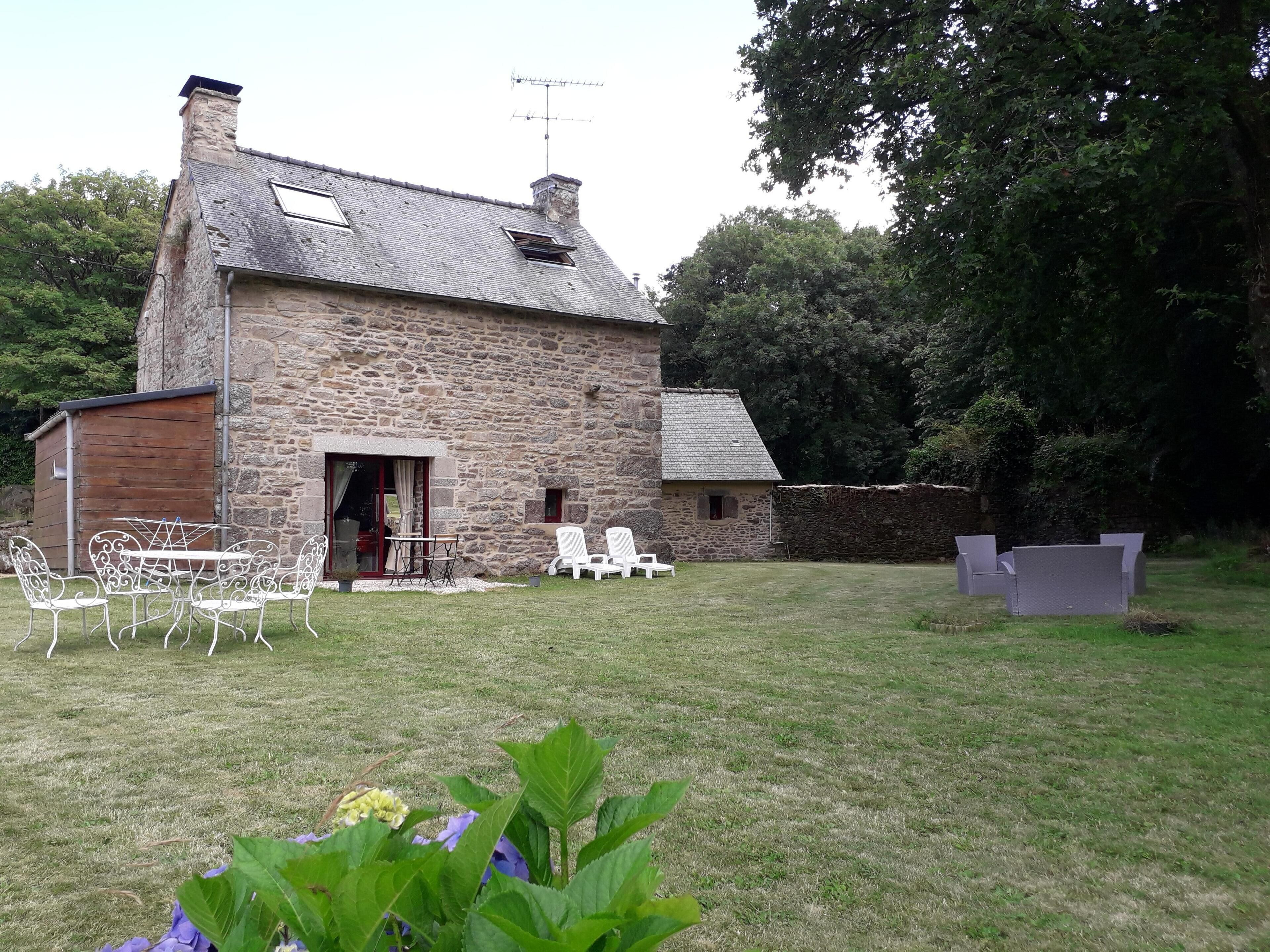 A stone building with a small patio area, a wooden shed, and a grassy yard.