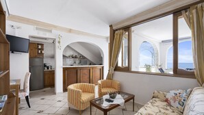 A living room with a sofa, two armchairs, a coffee table, and a TV. There is a kitchen in the background with a refrigerator, stove, and cabinets. - Mare - Positano Center - Guest 4+1 People in 2 Bedrooms, 2 Bathrooms - AC & WiFi (Positano)