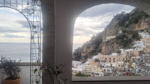 A coastal view through an arched window with a balcony, overlooking a hillside with colorful buildings. - Mare - Positano Center - Guest 4+1 People in 2 Bedrooms, 2 Bathrooms - AC & WiFi (Positano)