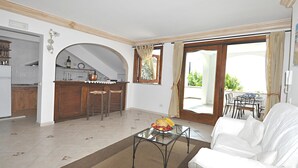 A living room with a white sofa, a glass coffee table with fruit, a kitchen with wooden cabinets, and a balcony with a table and chairs. - Mare - Positano Center - Guest 4+1 People in 2 Bedrooms, 2 Bathrooms - AC & WiFi (Positano)