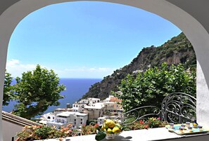 Un balcon donnant sur un village côtier, un vase rempli de citrons et une table avec des tasses et des soucoupes.