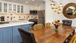 A modern kitchen with white cabinets, a stainless steel refrigerator, and a wooden dining table with chairs.
