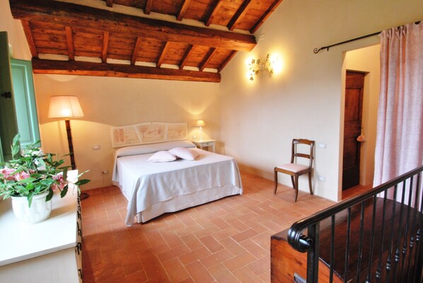 A bedroom with a wooden ceiling, a bed with white bedding, a chair, and a potted plant.