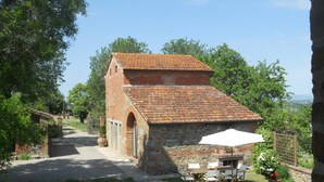 A rustic stone building with a tiled roof, a paved pathway leading to it, and a table with chairs outside.