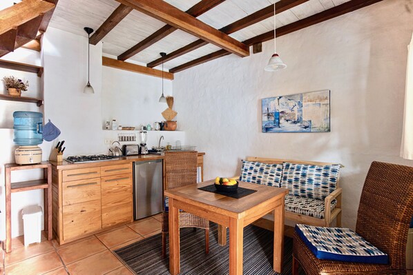 A compact kitchen with wooden cabinets, a dining table, and a wicker chair.