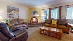 A cozy living room with leather sofas, a fireplace, and a large window with curtains. - Enzian 116 - 3 Bedroom Silver (Vail)