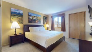 A hotel room with a large bed, two bedside tables with lamps, a wooden wardrobe, and two landscape paintings on the wall. - Enzian 116 - 3 Bedroom Silver (Vail)