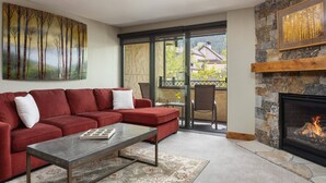 Una sala de estar con un sofá rojo, una mesa de centro, una chimenea y un ventanal con vistas a edificios y árboles.