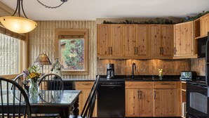 Una cocina con armarios de madera, lavavajillas, cafetera y comedor con mesa y sillas.