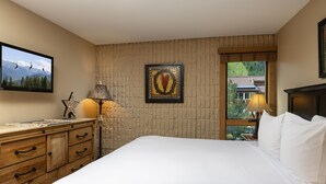 Una habitación de hotel con cama, tocador, un cuadro enmarcado, ventana y lámpara.