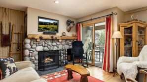 Una sala de estar acogedora con una chimenea de piedra, un televisor montado encima y una zona de estar cómoda con un sofá y sillones.