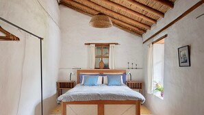 A bedroom with a wooden bed, a bedside table, a hanging light, a window with curtains, and a wall-mounted picture. - Romantic Cottage in a beautiful garden in  the Historic  Center of Quito (Quito)