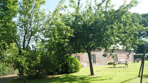 Een gazon met een stenen gebouw, picknicktafels en bomen.