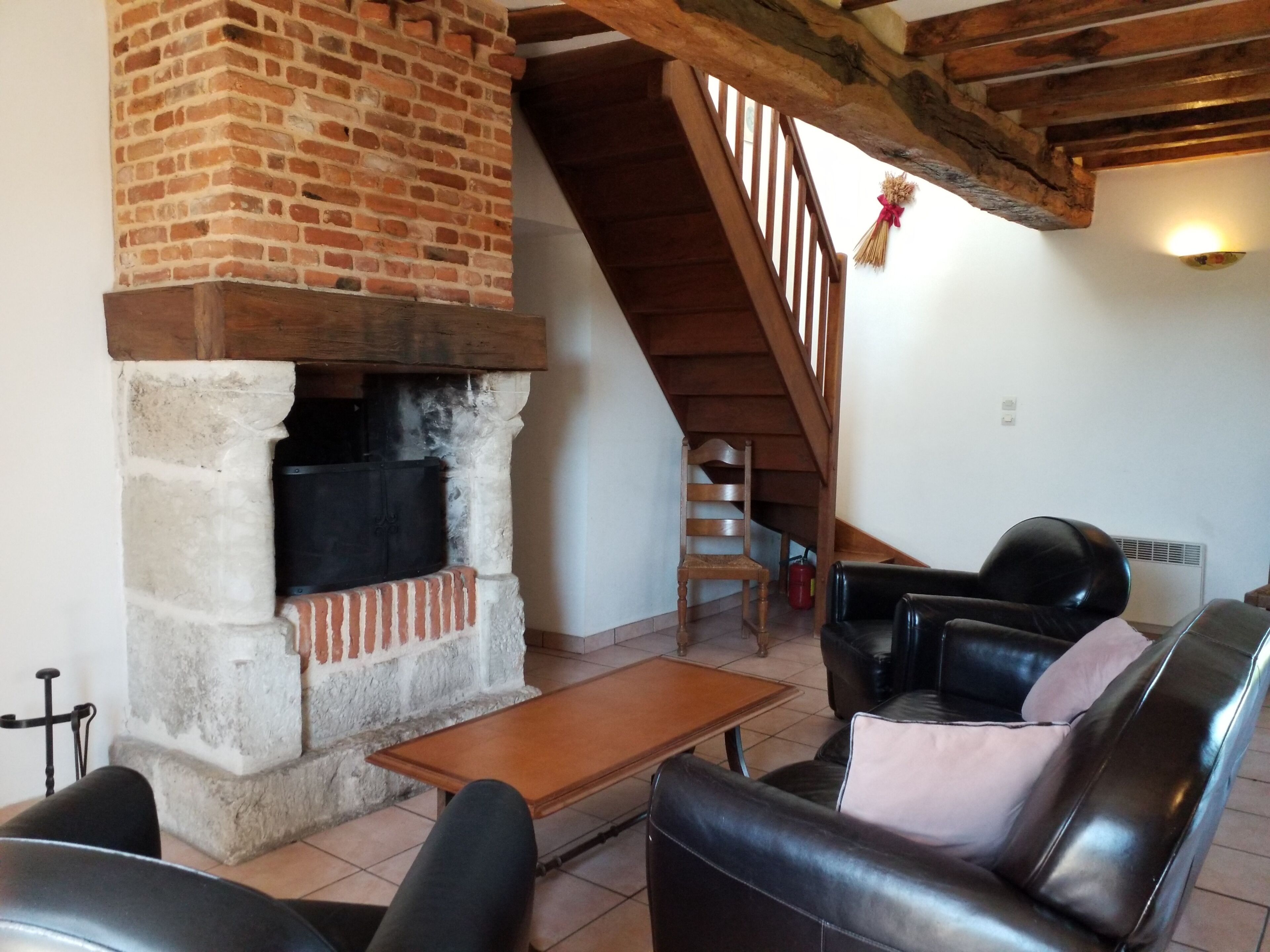 A living room with a fireplace, leather furniture, a wooden staircase, and a tiled floor.