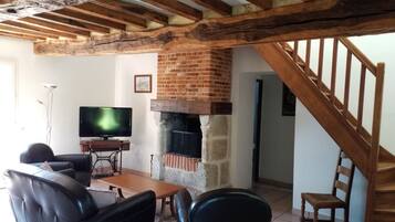 A living room with a fireplace, wooden beams, a television, and leather furniture.