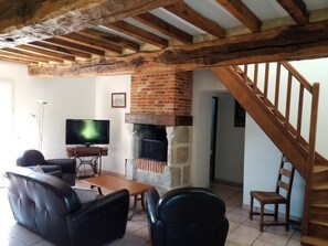 Una sala de estar con chimenea, vigas de madera, televisor y mobiliario de cuero.