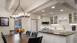 Une cuisine moderne avec des meubles blancs, un îlot central et un coin repas comprenant une table et des chaises en bois.