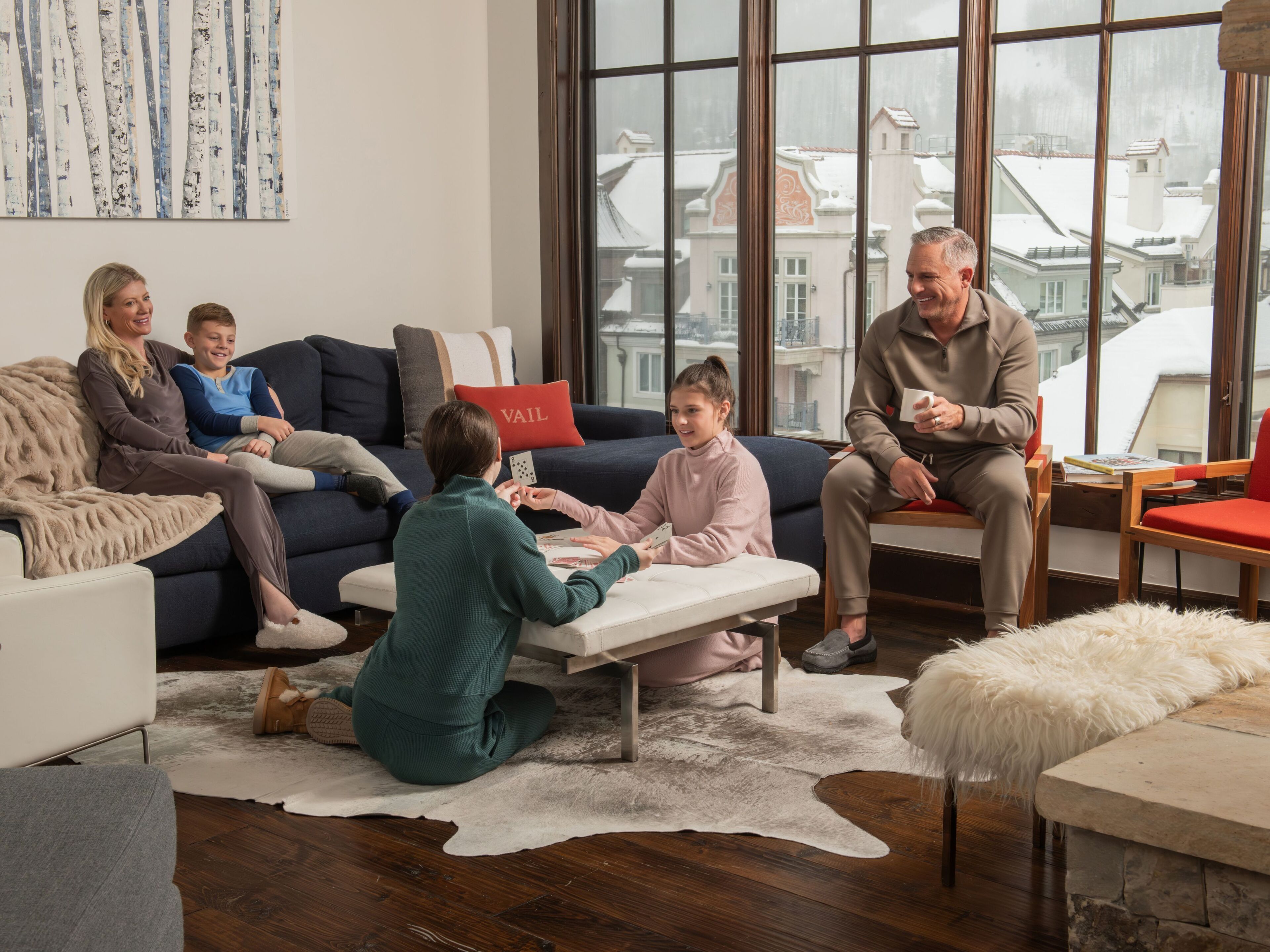 Gather your family in this inviting living room, where floor-to-ceiling windows frame snowy alpine rooftops and cozy modern furnishings invite connection and laughter after a day on the mountain.