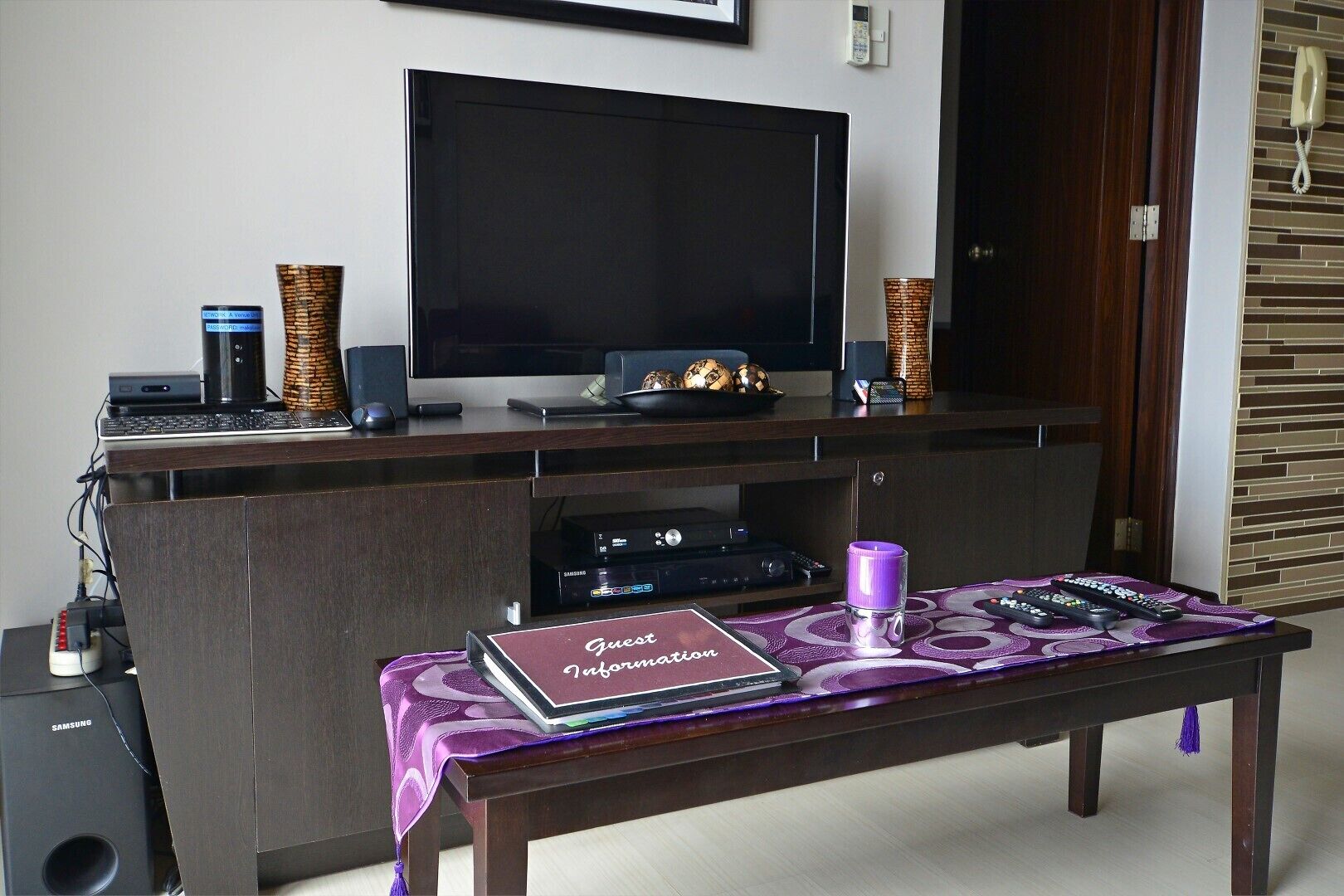 A living room with a flat-screen TV, a sound system, and a coffee table with a guest information booklet.