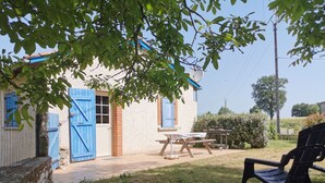 Une maison de campagne avec une porte bleue, un petit patio avec une table et des chaises, et une cour couverte d’herbe.