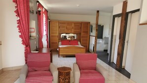 Une chambre à coucher comprenant un lit, deux fauteuils, une petite table et une armoire en bois.