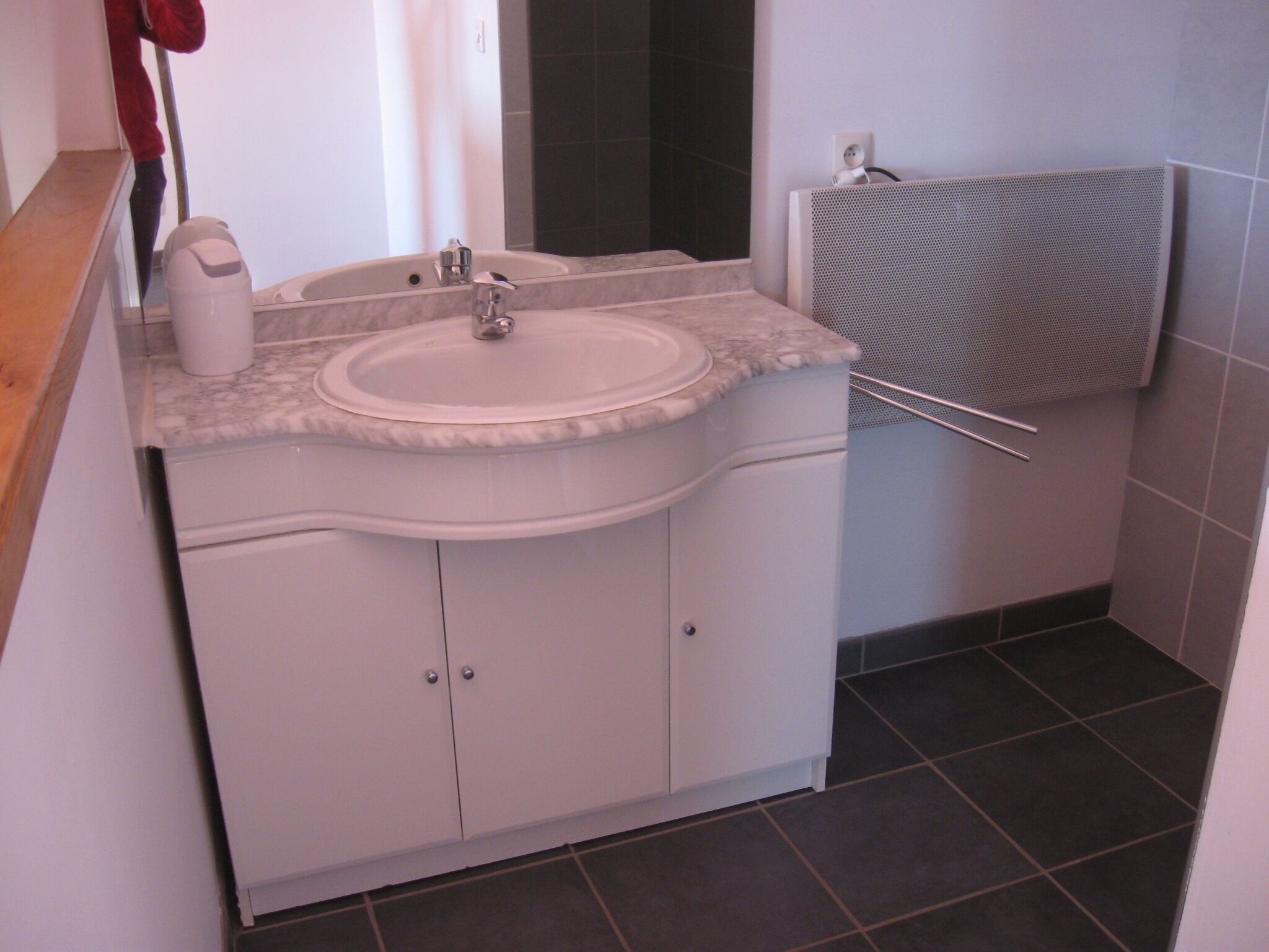A bathroom with a white sink, a mirror, a towel rack, and a shower area.
