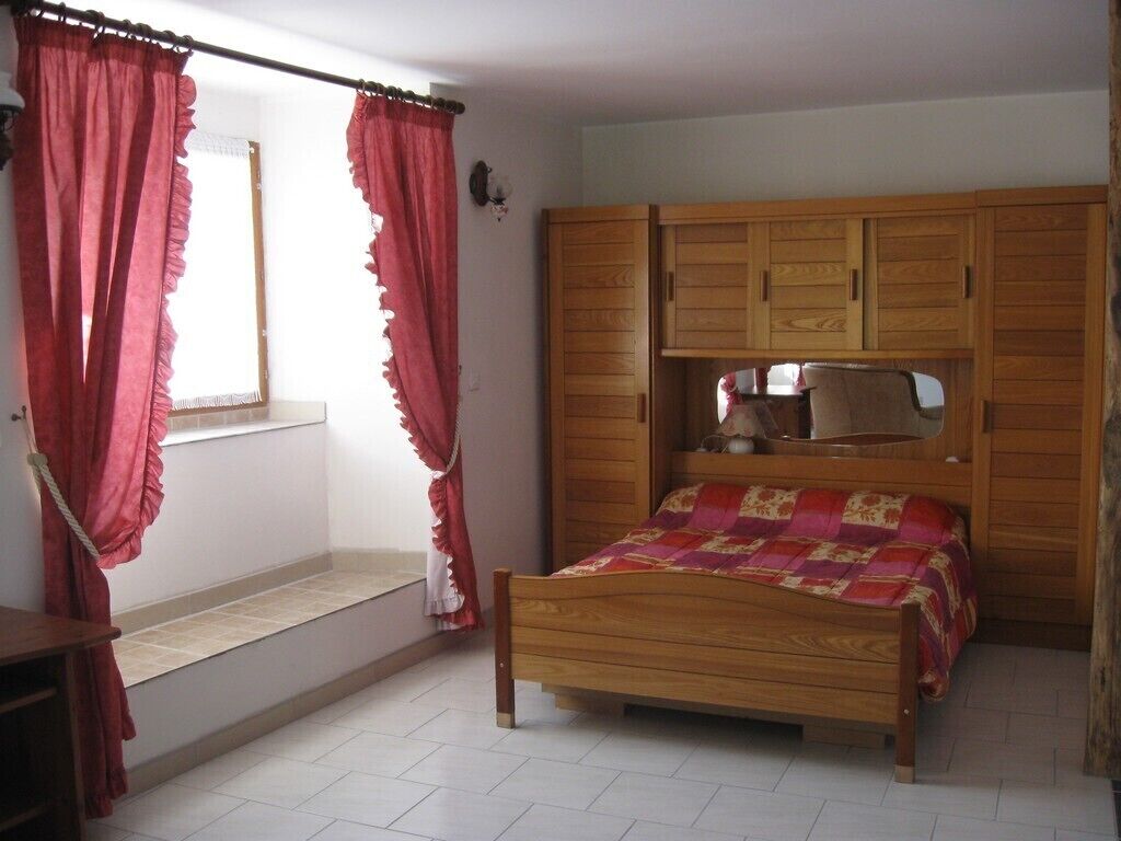 A bedroom with a wooden bed, a built-in wardrobe, and a window with curtains.