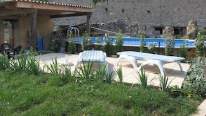 Un patio con piscina, sillones de descanso y un edificio de piedra.