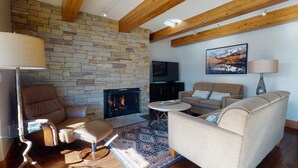 Una sala de estar acogedora con chimenea de piedra, muebles de cuero y un televisor montado.