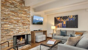 A modern living room with a stone fireplace, a mounted TV, a large abstract painting, and a cozy seating area. - Landmark 402 - 2 Bedroom Diamond (Vail)
