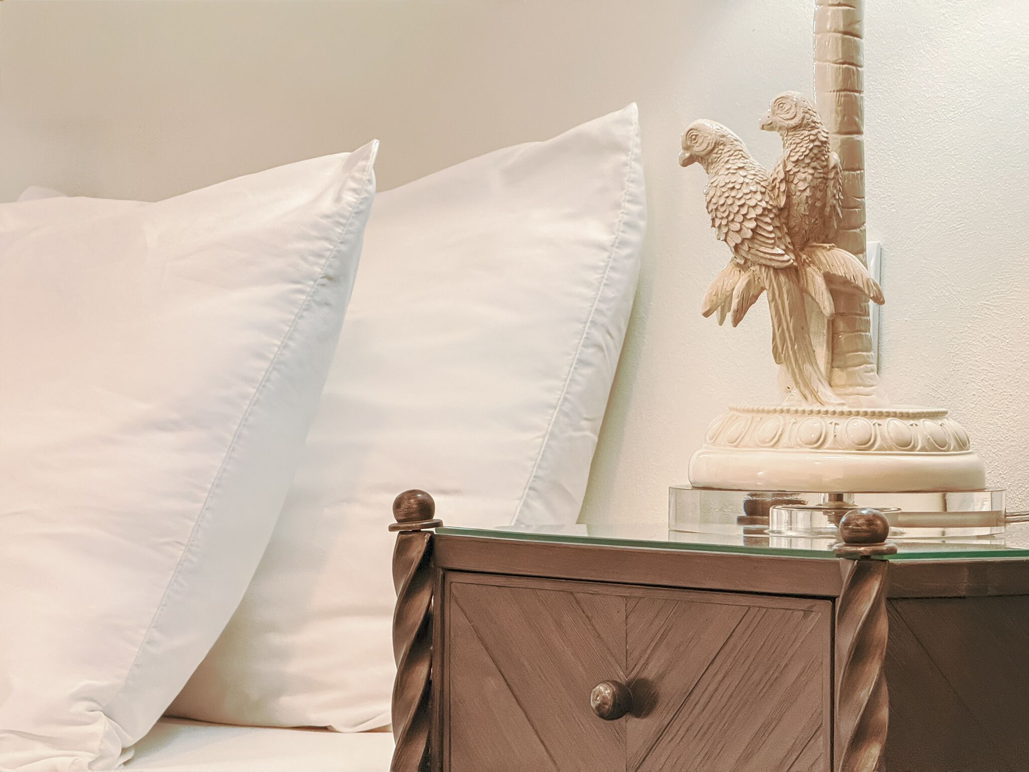 A bedroom with a bed, pillows, a nightstand, a decorative bird sculpture, and a mirror.