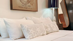 A bed with white bedding and starfish-patterned pillows, a framed artwork above the bed, and a floor lamp to the right.