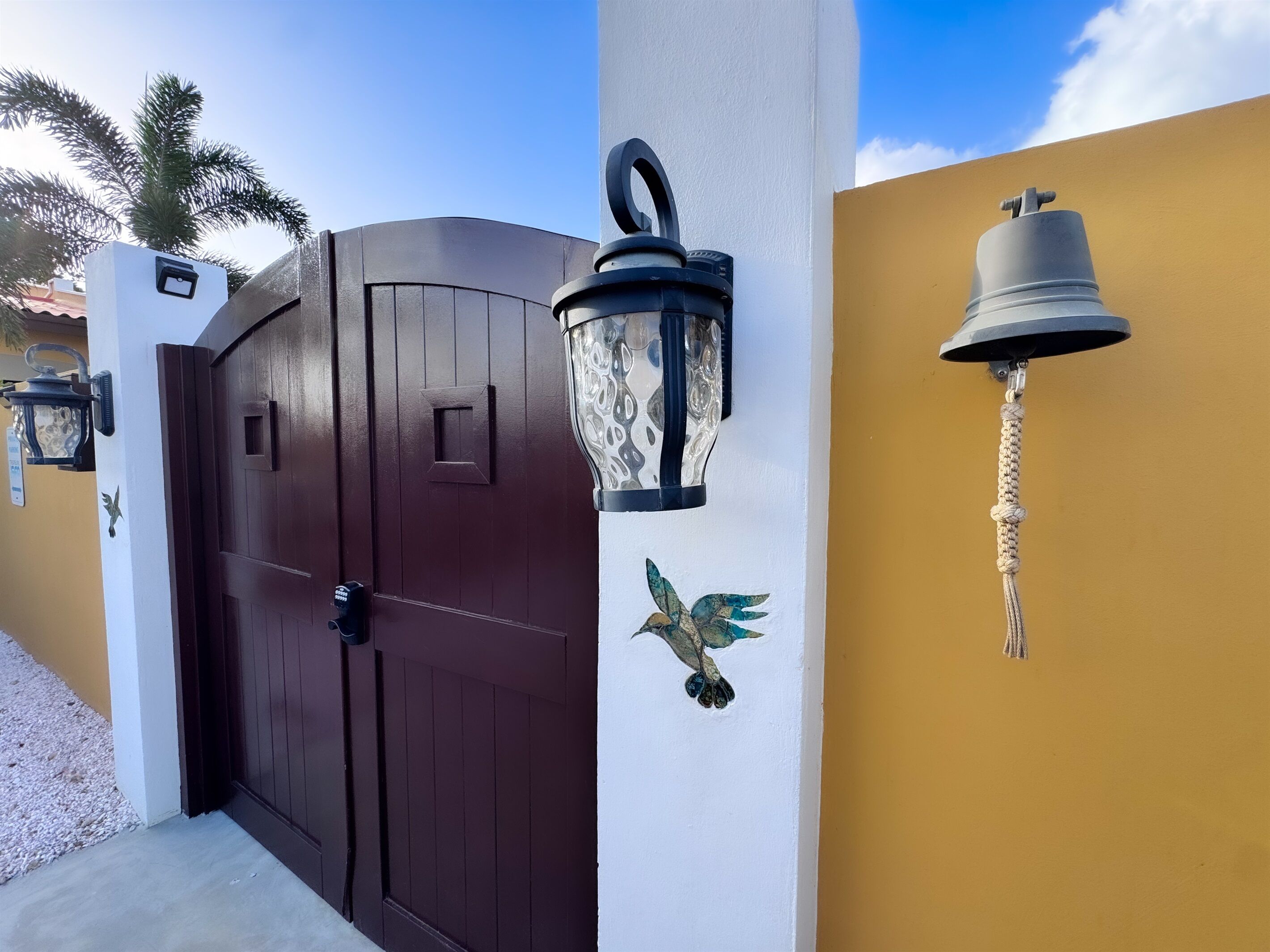 A gated entrance with a dark brown door, a decorative wall-mounted lantern, and a wall-mounted bell.