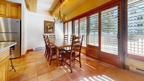 A dining area with a wooden table and chairs, a chandelier, and large windows with blinds. - Landmark 102 - 2 Bedroom Platinum (Vail)