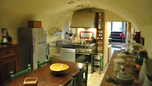 A compact kitchen with a central island, a refrigerator, and a dining area with a wooden table and chairs. - A Gorgeous Large Flat in Trastevere with a Beautiful Terrace (Roma)