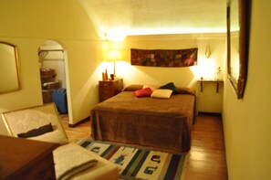 Quarto com uma cama de solteiro, mesa de cabeceira, abajur e uma pequena mesa.