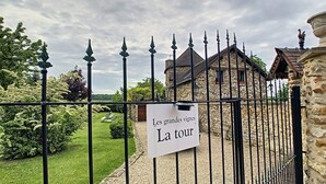 A sign reading "Les grandes vignes La tour" at a gated entrance with a stone building and a well-maintained garden in the background. - Holiday home " la tour 2 étoiles "Normandie (Saint-Étienne-Sous-Bailleul)