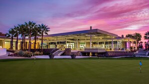 A modern building with a glass facade, palm trees, and a golf course in the foreground. - LOVE ... and MISCHIEF in Historic Twin Palms (Palm Springs)