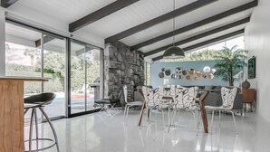 A modern dining area with a stone wall, large windows, and a ceiling with exposed beams. - LOVE ... and MISCHIEF in Historic Twin Palms (Palm Springs)