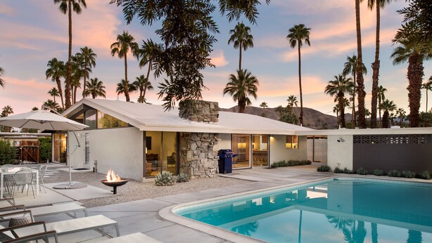 A modern outdoor pool area with a stone fireplace, lounge chairs, and a stone wall. - LOVE ... and MISCHIEF in Historic Twin Palms (Palm Springs)