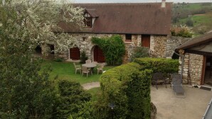 A stone house with a tiled roof, a stone porch, and a small garden with a table and chairs. - Vacation home Normandy "les voûtes 2 stars (Saint-Étienne-Sous-Bailleul)