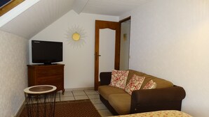 Une petite pièce chaleureuse, avec un téléviseur posé sur un meuble en bois, un canapé agrémenté de coussins à motifs floraux et un décor représentant un soleil accroché au mur.