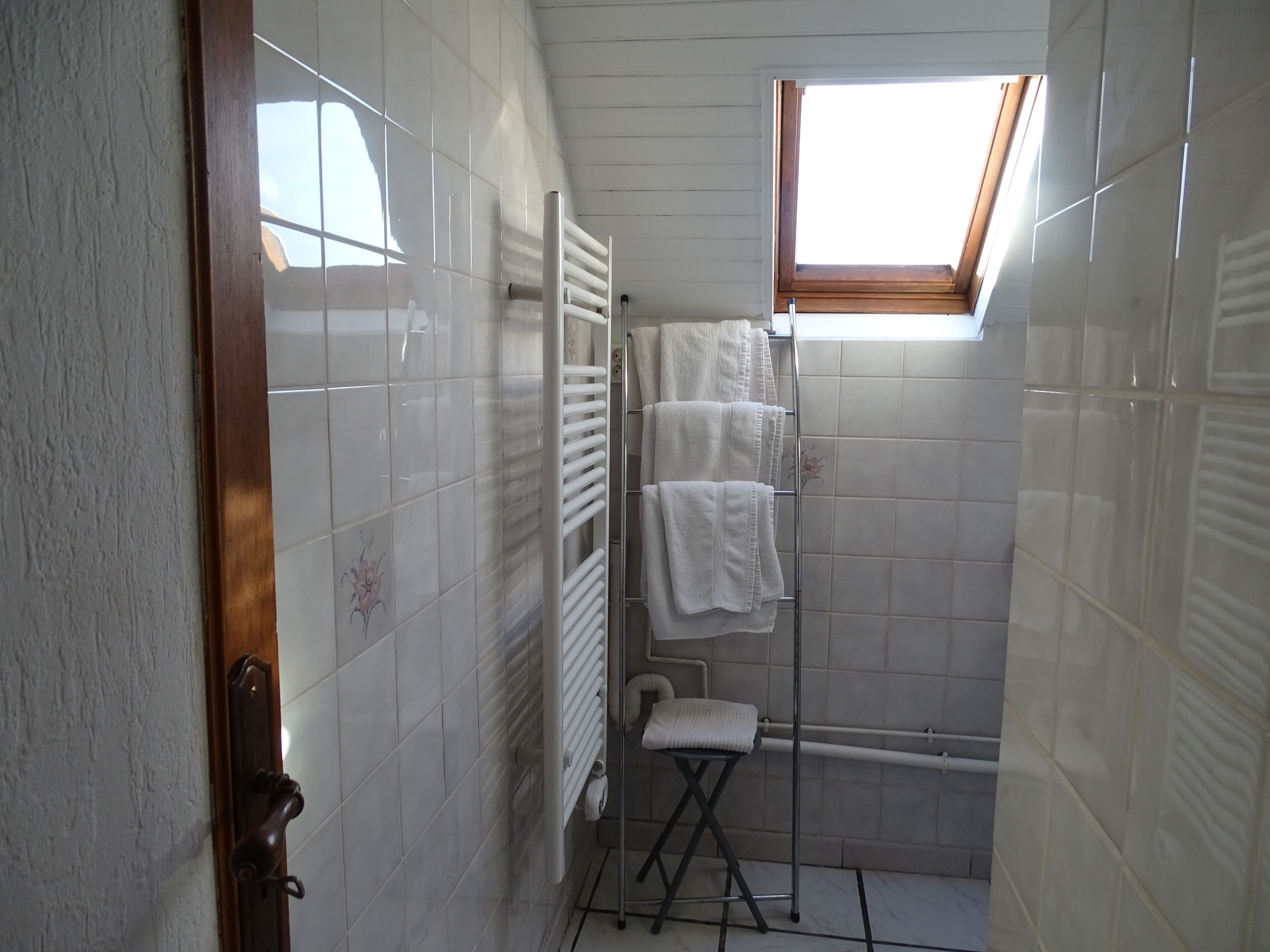 Un bagno piccolo con piastrelle, una finestra, un appendi asciugamani e un termosifone.