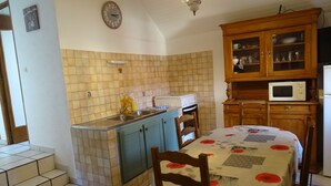Une cuisine avec un mur recouvert de carreaux, un meuble en bois doté de portes en verre, un four à micro-ondes et une table recouverte d’une nappe à motifs floraux.